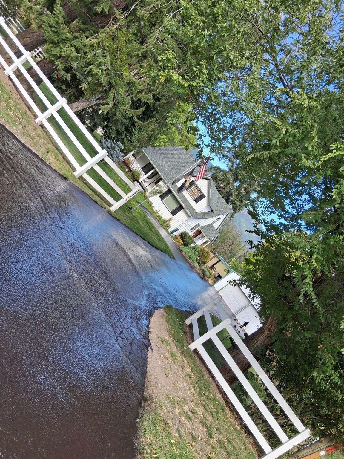 Dark driveway beside a white fence and landscaped residential property.